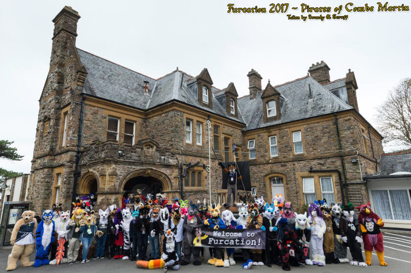 Furcation 2017 group photograph featuring fursuiters with the old stone built Combe Martin club house in the background.