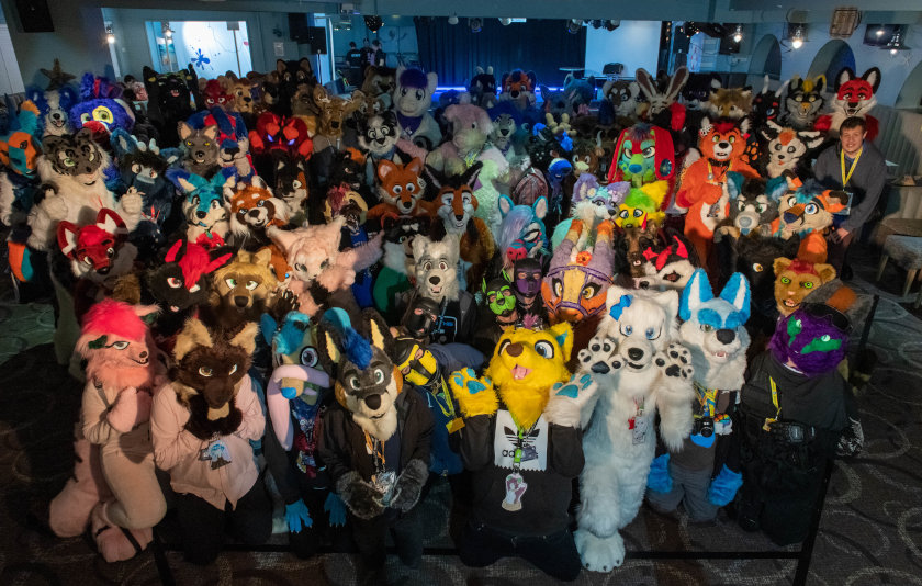 Furcation 2019 one of many group photographs featuring both fursuiters and none taken in the club house on the dance floor area with main stage in distant background.